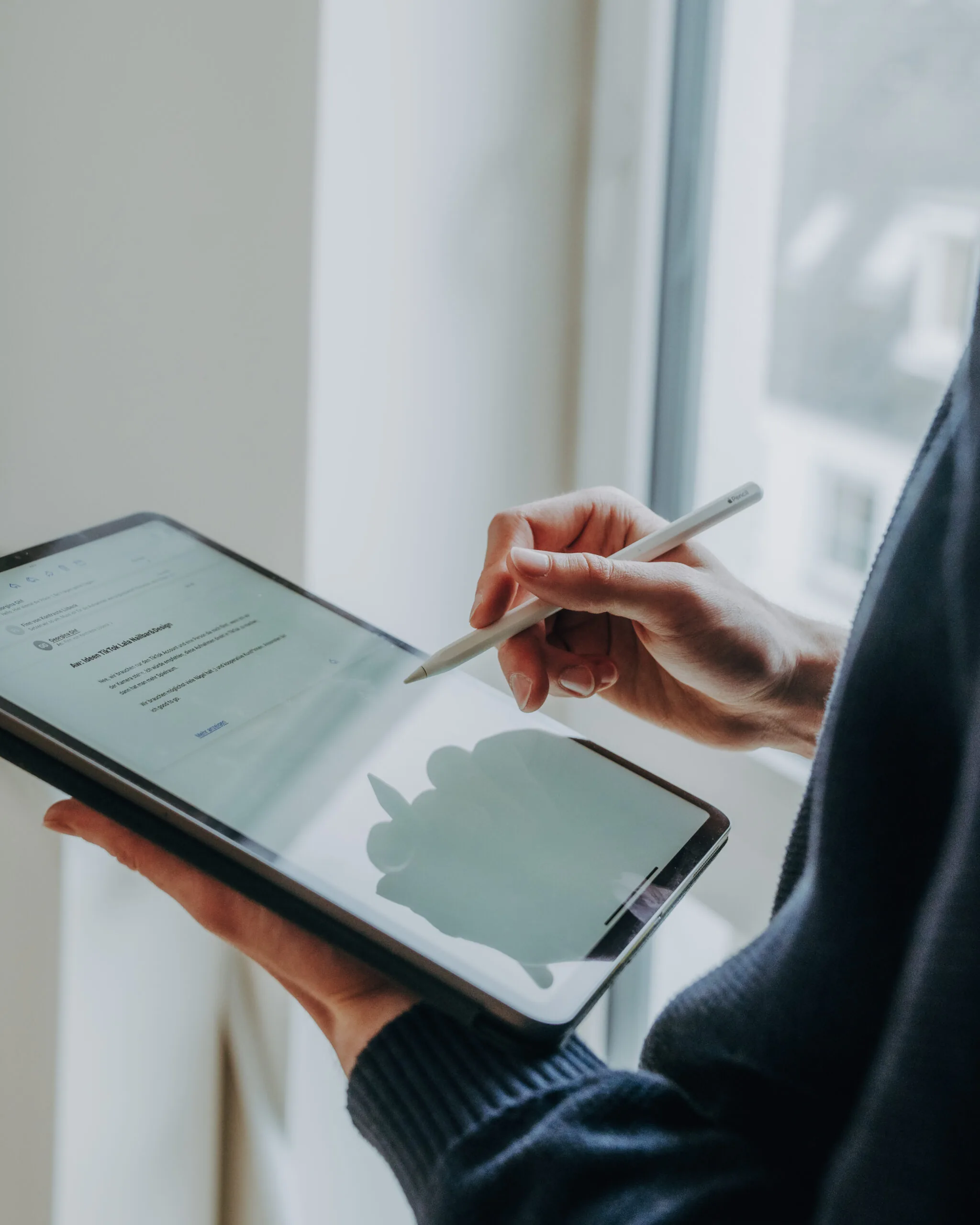 Eine Person hält ein Tablet und schreibt mit einem Apple Pencil auf dem Bildschirm, der einen Entwurf für TikTok-Inhalte zeigt.