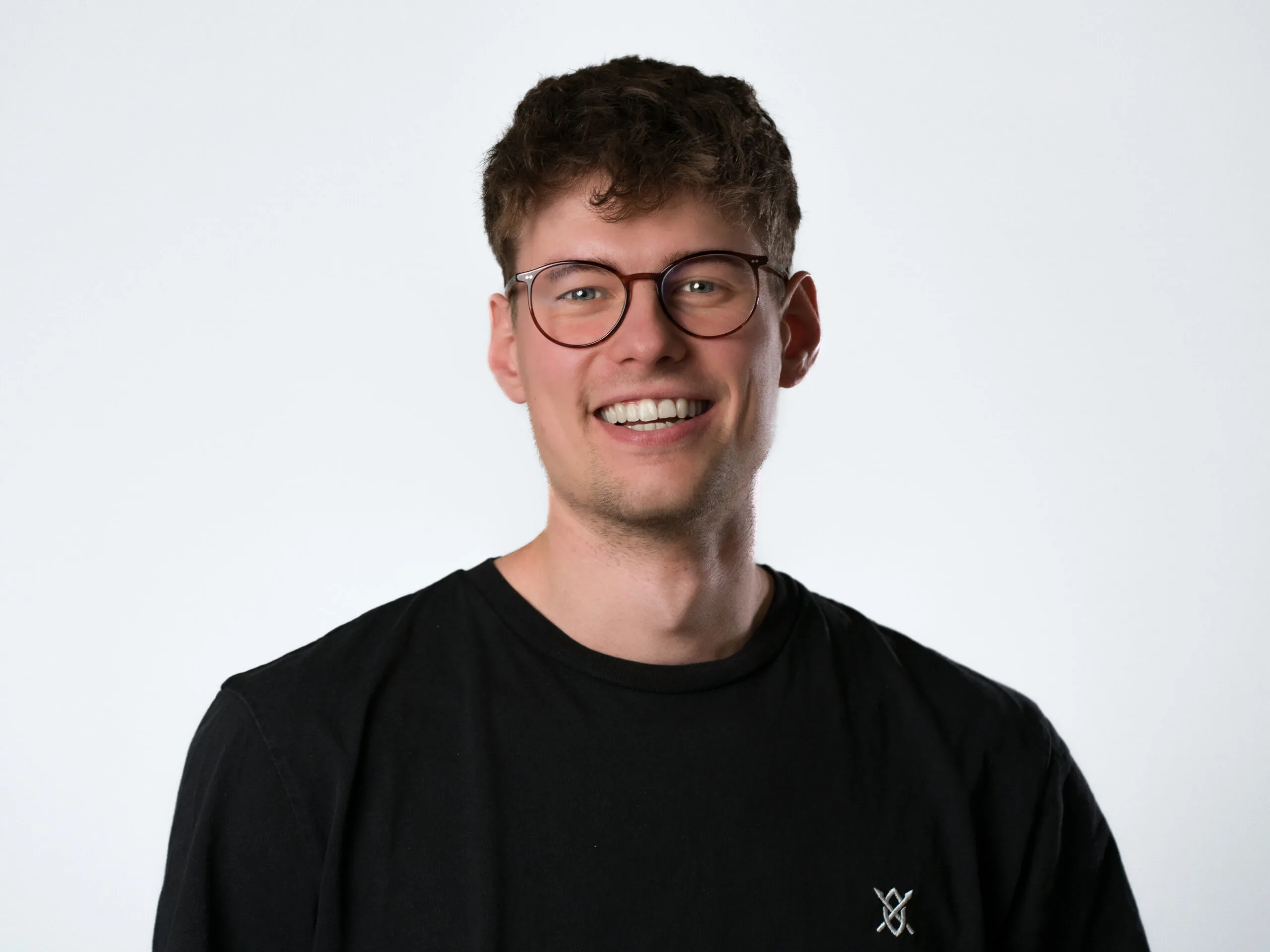 Porträt von Finn Robens, einem jungen Mann mit Brille und lockigem Haar, der lächelnd in die Kamera blickt.